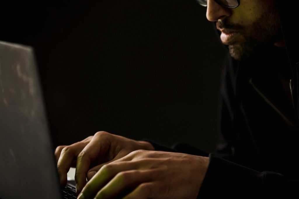 Close-up of a person typing on a laptop in a dark environment.