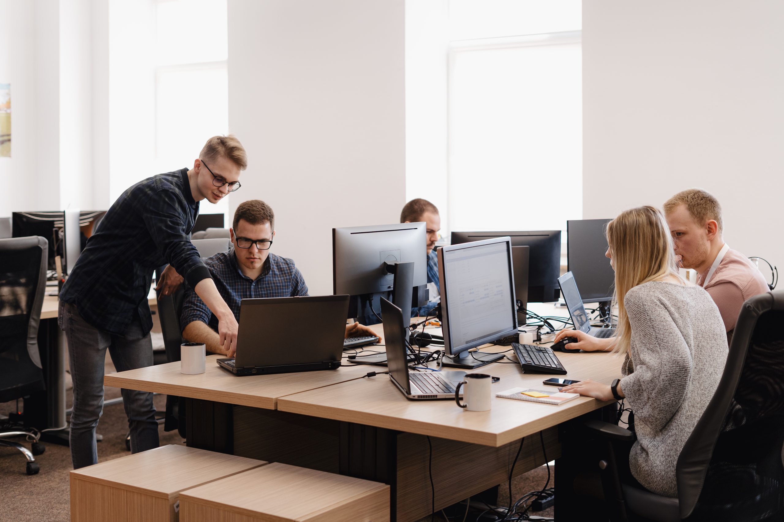 IT team collaborating in an office, reviewing code and system updates on multiple computer screens.